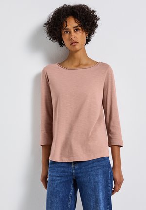 Un haut rose vif à manches trois quarts avec un col rond, fabriqué en tissu doux, associé à un jean en denim bleu. Texture lisse, coupe décontractée.