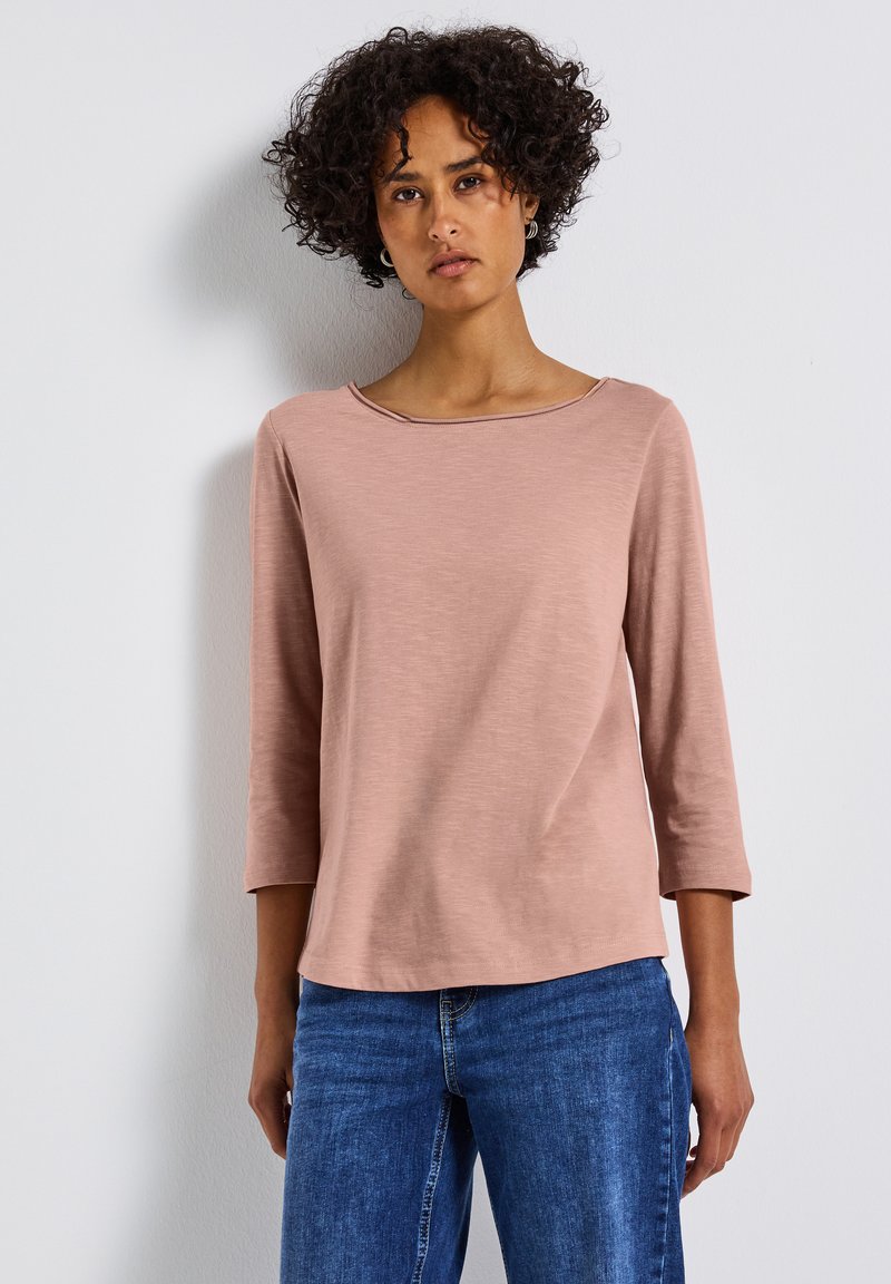 Top rosa con mangas tres cuartos y escote redondeado, hecho de una tela suave, combinado con jeans de denim azul. Textura suave, ajuste relajado.