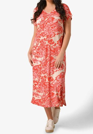 Kobieta w różowo-koralowej sukience midi w kwiatowy wzór, z krótkimi rękawami, nosząca białe sneakersy na platformie z sznurowaniem.