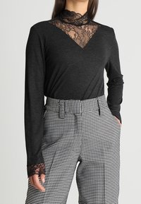 Woman wearing black long-sleeve top with lace details on collar and cuffs, paired with high-waisted black and white houndstooth pants.