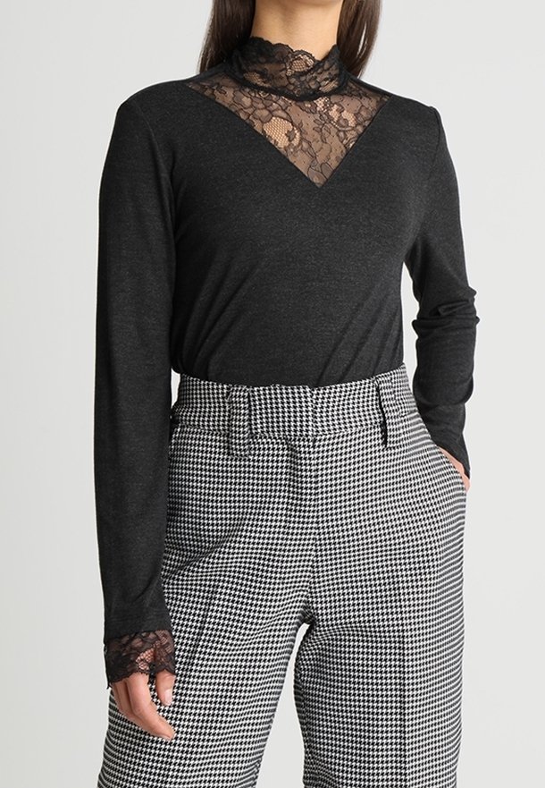 Woman wearing black long-sleeve top with lace details on collar and cuffs, paired with high-waisted black and white houndstooth pants.