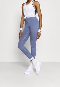 Light blue leggings with contrasting white stitching, fitted design, and Nike logo. Paired with a white tank top and white athletic shoes.