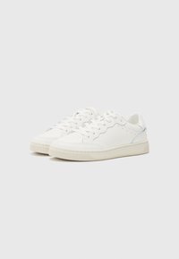 Hvite sneakers med en glatt læroverdel, distinkt bølgete design, perforeringer på tåen, og en teksturert gummisåle.