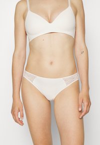 Beige bh og matchende truse i sett med glatt stoff, blonder detaljer på sidene og justerbare stropper. Enkel og minimalisk design.