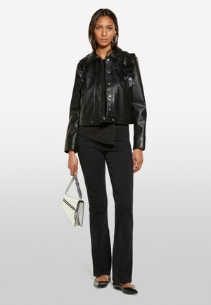 Veste en cuir noir courte avec des appliqués floraux sur les épaules, associée à un pantalon noir et des ballerines, tenant un sac à main en argent.