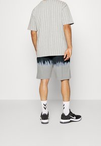 Camicia a maniche corte grigia a righe, pantaloni a shorts tie-dye grigi e neri, calzini bianchi con chevron neri, scarpe da ginnastica nere con accenti bianchi.