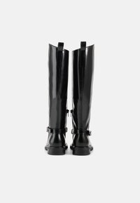 Botas pretas até o joelho com acabamento brilhante, apresentando duas tiras ajustáveis e uma sola robusta. A vista traseira exibe costuras verticais e alças.