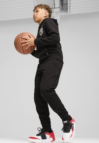 Juodas kapučino megztinis ir sportinės kelnės su krepšiniu, derinamos su daugiakuklėmis sportinėmis avalynėmis, turinčiomis raudonų, baltų ir juodų akcentų. Lygus paviršius.