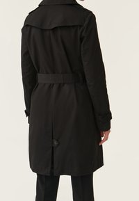 Czarny płaszcz trench z tylnym paskiem, szerokimi klapami i zapięciem na guzik przy końcu. Wykonany z gładkiego materiału o klasycznym fasonie.