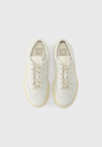 Λευκά δερμάτινα αθλητικά παπούτσια με απαλές κίτρινες πινελιές, με στρογγυλεμένη μύτη, σχέδιο με κορδόνια και υφή στη σόλα. Το λογότυπο της μάρκας είναι ορατό στην εσωτερική σόλα.