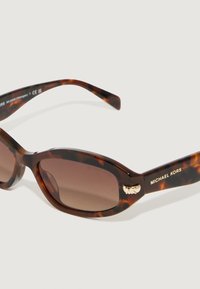 Occhiali da sole in tartaruga con lenti ovali, sfumatura marrone, dettagli dorati sulla parte frontale, con il marchio "MICHAEL KORS" sulla stanghetta.