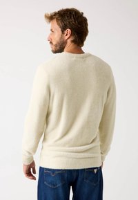 Suéter color crema con un acabado suave y texturizado, con mangas largas y un escote redondo, combinado con jeans de color azul oscuro.