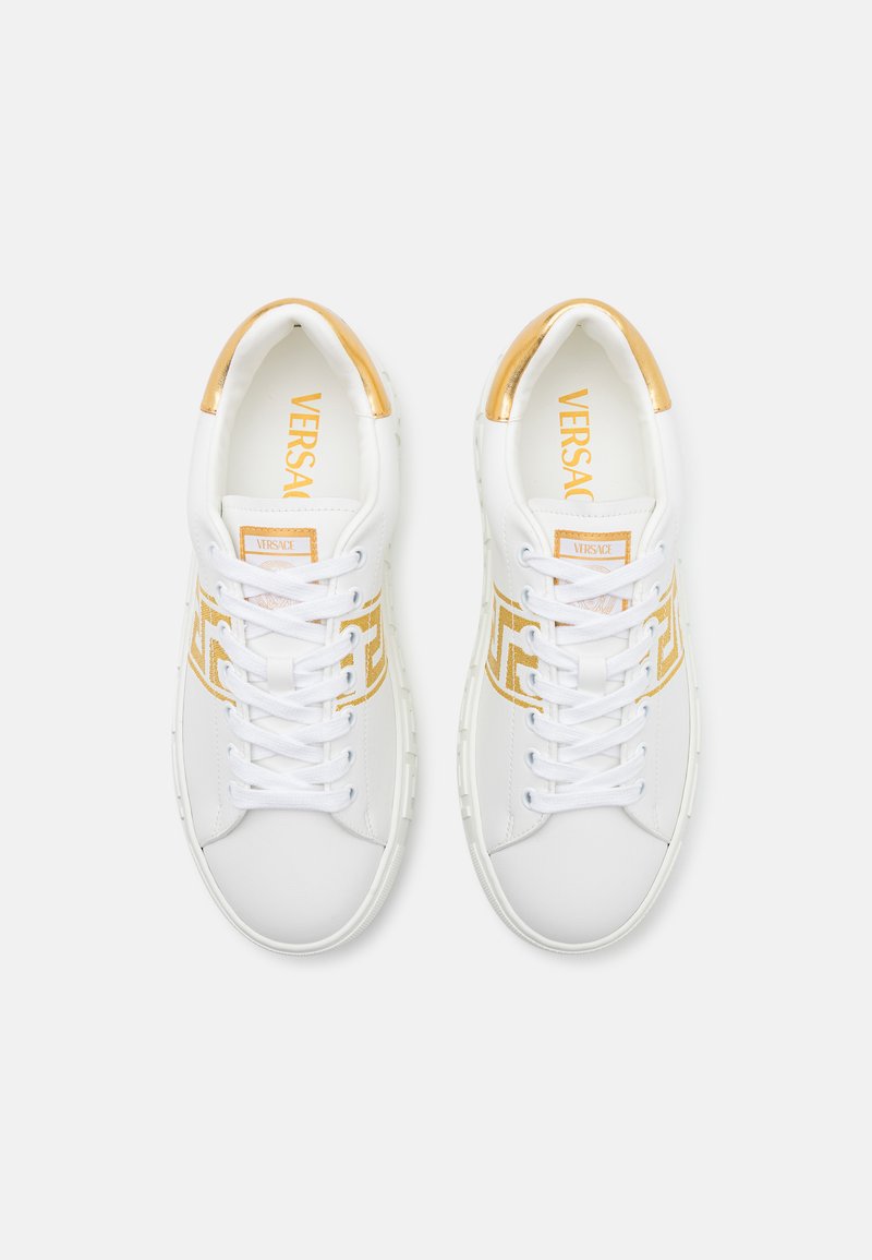 Sneakers bianchi con accenti dorati, caratterizzati da una tomaia in pelle liscia, chiusura con lacci e dettaglio del logo impresso. Design a punta rotonda.