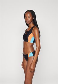 Conjunto de bikini negro que incluye un top corto con paneles laterales en naranja y azul, y braguitas a juego con detalles de colores similares.