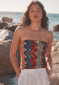 Top senza spalline con un motivo ondulato in rosso, blu, giallo e bianco. Il materiale sembra leggero con arricciature sui lati.