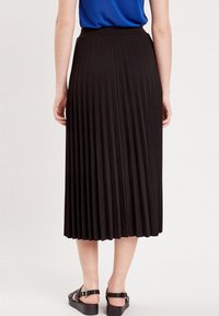 Jupe midi plissée noire avec une taille élastique, texture lisse. Portée avec un top bleu et des sandales à plateforme noires.