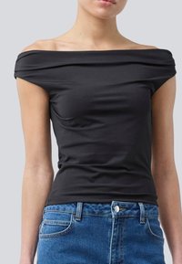Zwarte off-shoulder top van gladde stof, met een aansluitend ontwerp en zachte draping bij de halslijn. Gecombineerd met blauwe denim jeans.