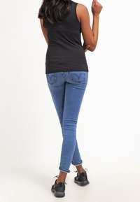Top smanicato nero, jeans skinny blu medio e sneakers nere. I jeans presentano un classico design della tasca posteriore e una leggera usura sull'orlo.