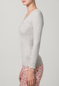 Gray long-sleeve top with a v-neckline, made of ribbed fabric, styled with a fitted silhouette. Worn with pink pants featuring navy polka dots.