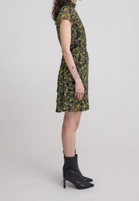 Vestido floral corto con fondo negro, patrón floral amarillo y verde, mangas con volantes y combinado con botas negras hasta el tobillo. Textura suave.