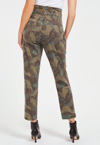 Camo-gepatte broek in groen, bruin en blauw. Hoge taille met een rechte pijp en enkel lengte, gecombineerd met zwarte hakken.