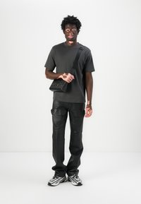 T-shirt noir, pantalon en cuir noir de style cargo et baskets noires et blanches à motifs. Sac bandoulière noir avec logo embossé.