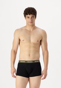 Boxer in cotone neri con design aderente, caratterizzati da una cintura verde oliva con il logo "HUGO". Tessuto morbido e lunghezza delle gambe corta.