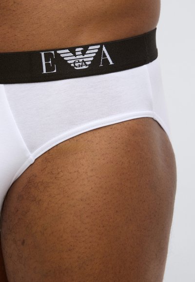 Mutande bianche in cotone con un bordo in vita scuro a contrasto che presenta un logo. Tessuto liscio, design aderente e dettagli di cuciture minimi.