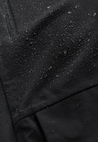 Sort vandtæt stof med en glat tekstur, med vanddråber på overfladen og subtile sømdetaljer.