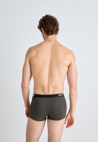 Schwarze Boxershorts mit einem gepunkteten Muster, ausgestattet mit einem schwarzen Bund, der "BOSS" beschriftet ist. Der Stoff scheint elastisch und eng anliegend zu sein.