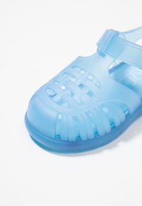 Hele sinine poolläbipaistev plastist sandaal, mille esiosas on kootud disain, kindel pahkluu rihm ja tekstureeritud tald.