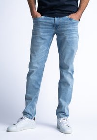 Lichtblauwe denim jeans met een slim fit, voorzien van vijf zakken en subtiele vervaging. Gecombineerd met witte sport schoenen.