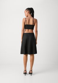 Sort crop top med tynde stropper, parret med en sort nederdel i knælængde. Nederdelen har en A-formet silhuet og en diskret lynlås bagpå.