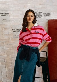 Rød- og rosa-stripete polo skjorte med hvit krage, kombinert med en høylands denim skjørt og en svart genser knyttet rundt livet.