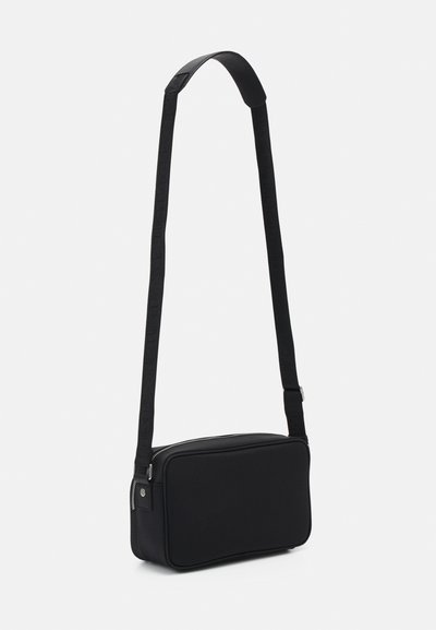 Bolso bandolera negro con un exterior de tela suave, forma rectangular, correa ajustable y cierre superior con cremallera.
