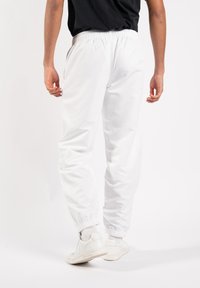 Witte joggingbroek met een elastische tailleband en opgestikte zoom, gemaakt van een glad materiaal, gedragen door iemand met witte sneakers.