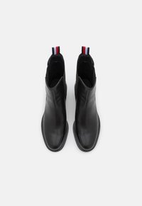 Botas de cuero negras hasta el tobillo con un acabado suave, punta afilada y paneles laterales elásticos. Presentan una etiqueta roja, blanca y azul en el talón.