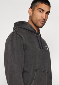 Sweatshirt à capuche gris charbon avec une poche kangourou, fermeture à cordon, et logo Champion blanc sur la poitrine, offrant une texture douce.