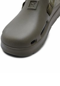 Olívazöld, sima műanyagból készült slip-on cipő, lekerekített orral, oldalán logóval és szellőzőlyukakkal.