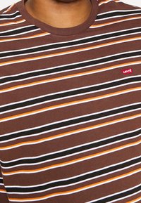 Camiseta de rayas marrón con líneas horizontales en blanco, negro y naranja, con cuello redondo y pequeño logotipo rojo de Levi's.