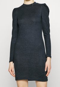 Mörkgrå långärmad klänning med en åtsittande siluett, tillverkad av mjukt material. Har subtila puffade axlar och en hög halsringning.