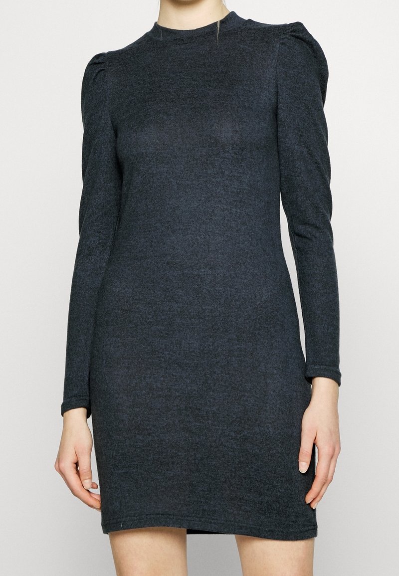 Mörkgrå långärmad klänning med en åtsittande siluett, tillverkad av mjukt material. Har subtila puffade axlar och en hög halsringning.