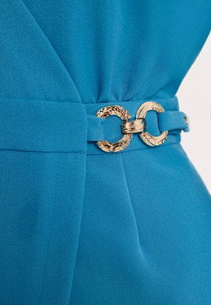 Niebieski pas materiałowy z teksturowaną złotą klamrą w kształcie podwójnego pierścienia, zapięty wokół talii ubrania.