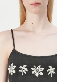 Canotta nera con spalline sottili, caratterizzata da ricami bianchi di motivi floreali e palme nella zona del petto. Tessuto morbido e leggero.