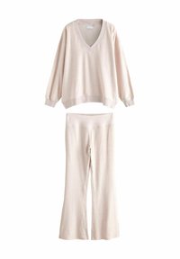 Jasno beżowy zestaw odzieży domowej składający się z rozpinanego swetra z dekoltem w serek i rozszerzanych spodni. Wykonany z miękkiego materiału o gładkiej fakturze.