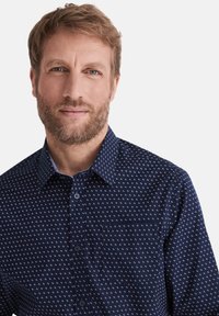 Navyblaues Hemd mit Knopfleiste und einem kleinen, wiederholten geometrischen Muster in Weiß und Rot. Mit einer Tasche auf der linken Seite und einem klassischen Kragen.