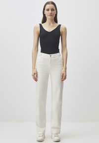 Top nero senza maniche abbinato a jeans bianchi a vita alta. I jeans hanno un taglio dritto, con chiusura a bottone e zip, e tasche laterali.