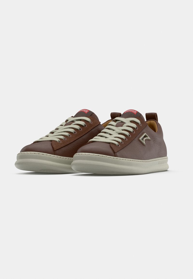 Brown leather sneakers with a smooth finish, contrasting light laces, rounded toe design, and a rubber sole. Features a logo on the side.