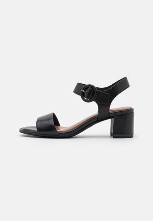 Mustat nahkasaappaat matalalla blokkikorkealla, avoimella varpaalla ja nilkkahihnalla, jossa on pyöreä solki.