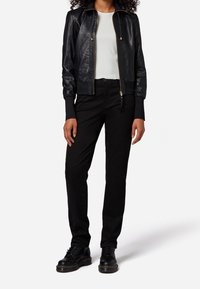 Černá kožená bomber bunda s žebrovanými manžetami, zapínáním na zip a bílým topem. Kombinováno s černými kalhotami a černými šněrovacími botami.